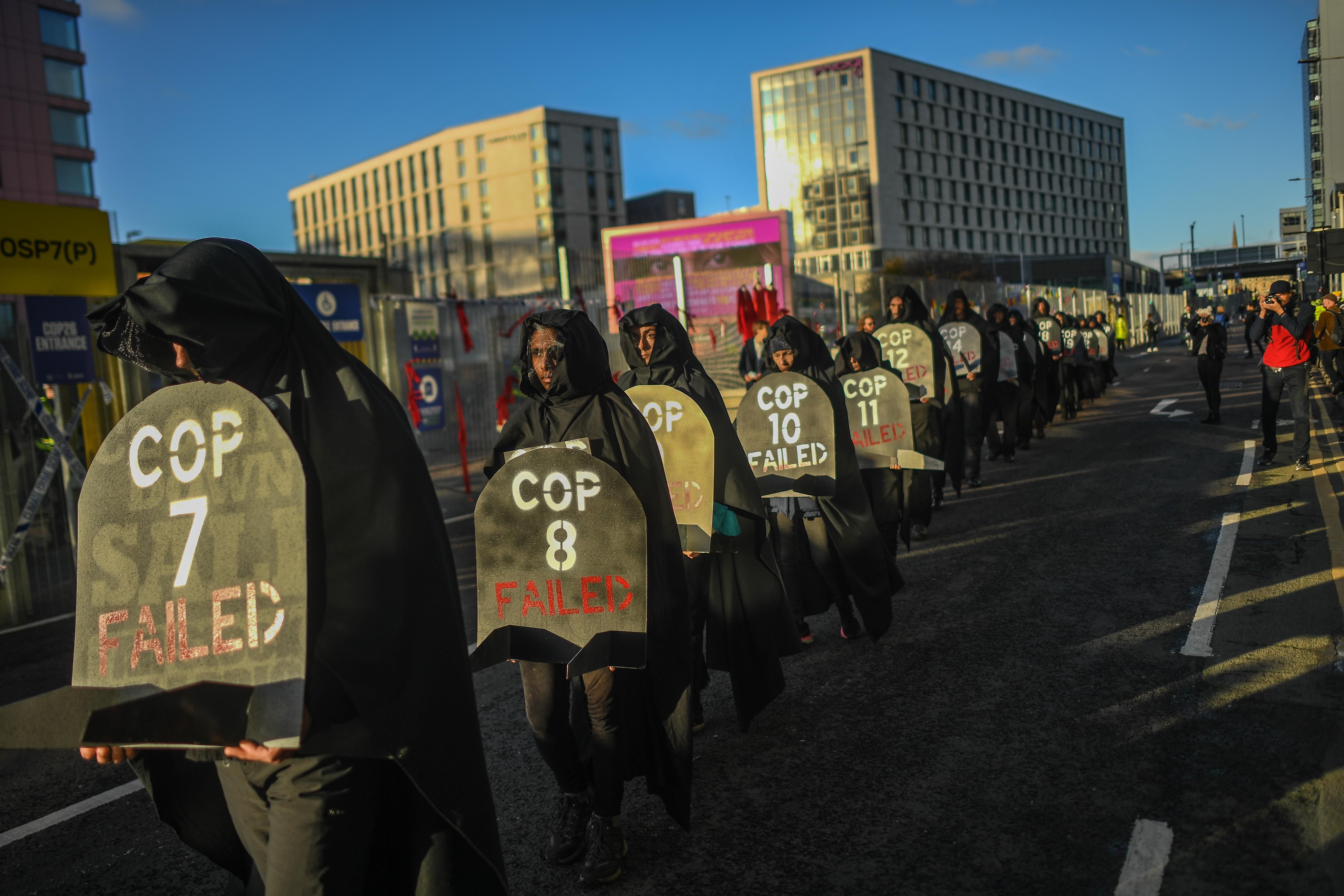 Protesters are seen carrying gravestones with the numbers of COP conferences claiming they have failed during a protest outside the entrance to the COP26 site