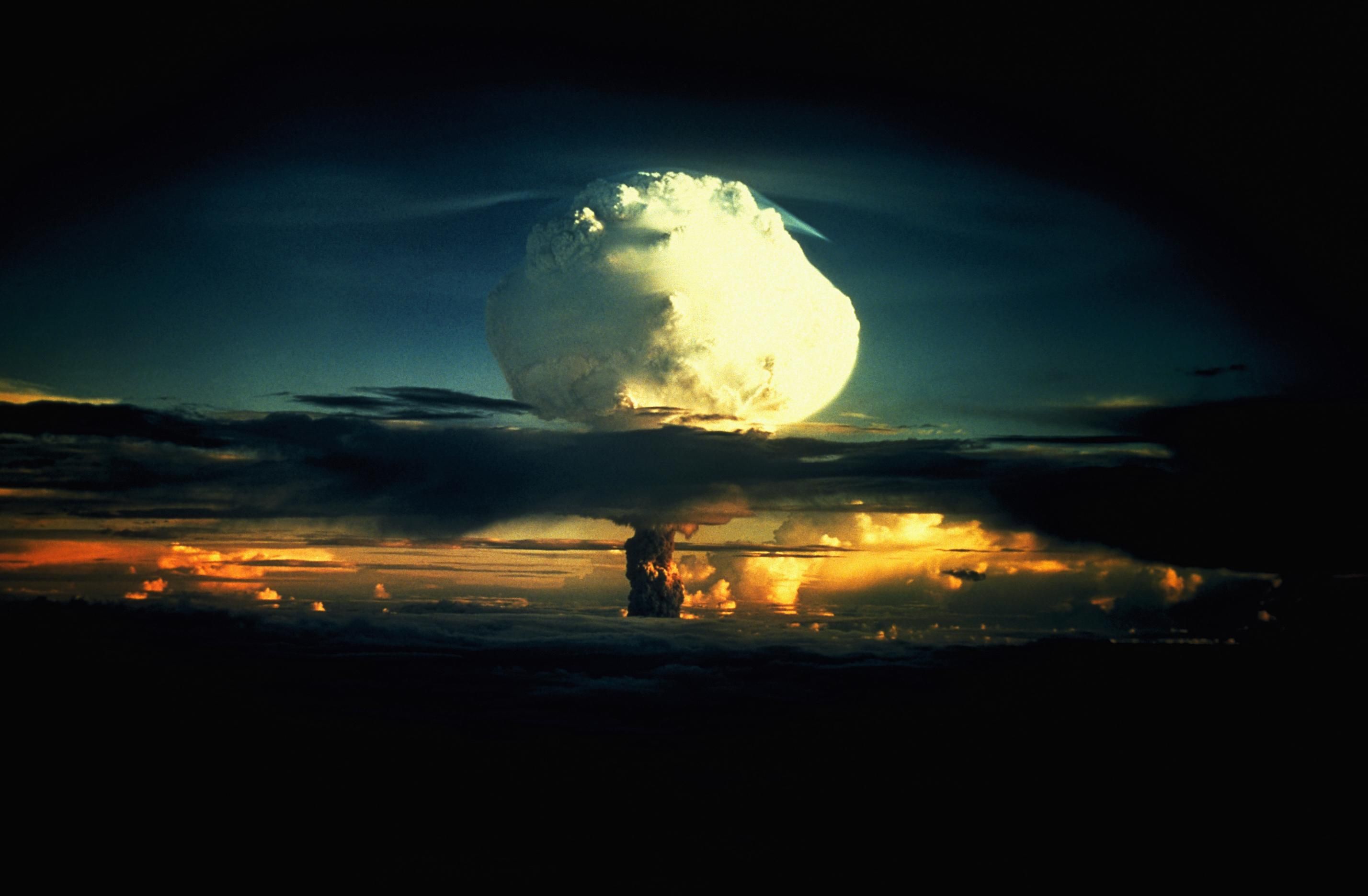 A billowing white mushroom cloud, mottled with orange, pushes through a layer of clouds during Operation Ivy, the first test of a hydrogen bomb