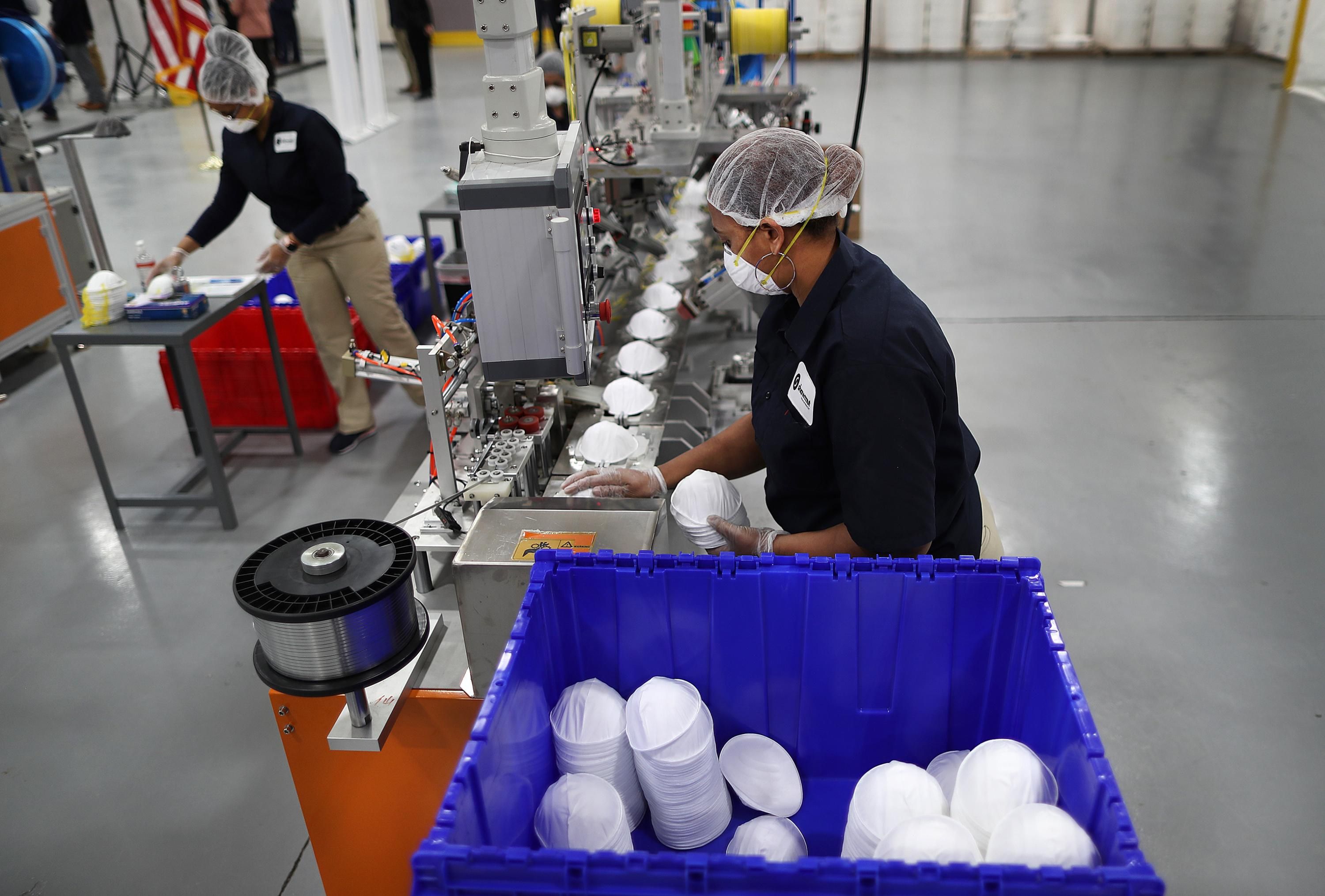 A worker gathers N95 masks off an assembly line