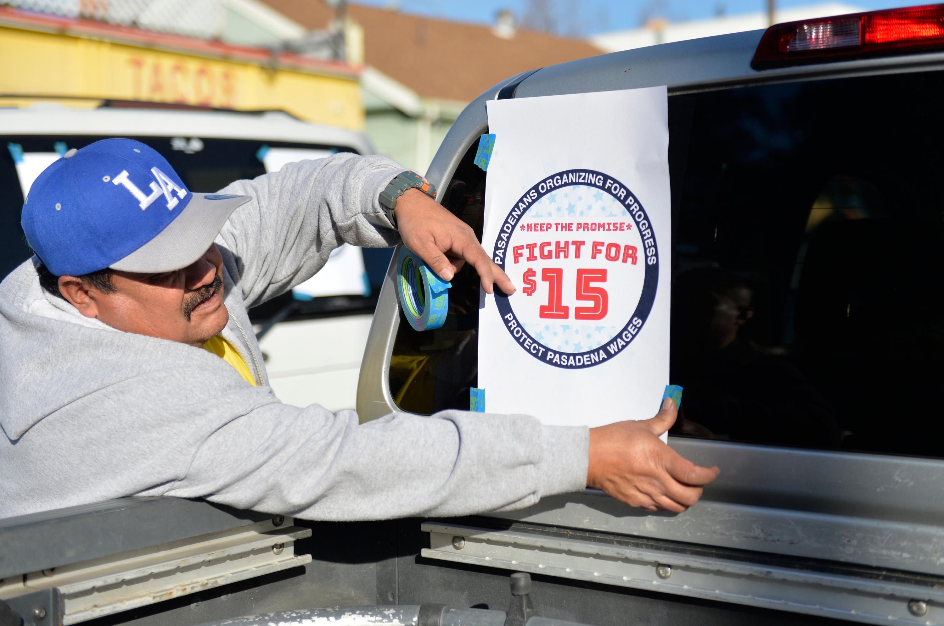 A demonstrator attaches a "Fight for $15" sign to his truck