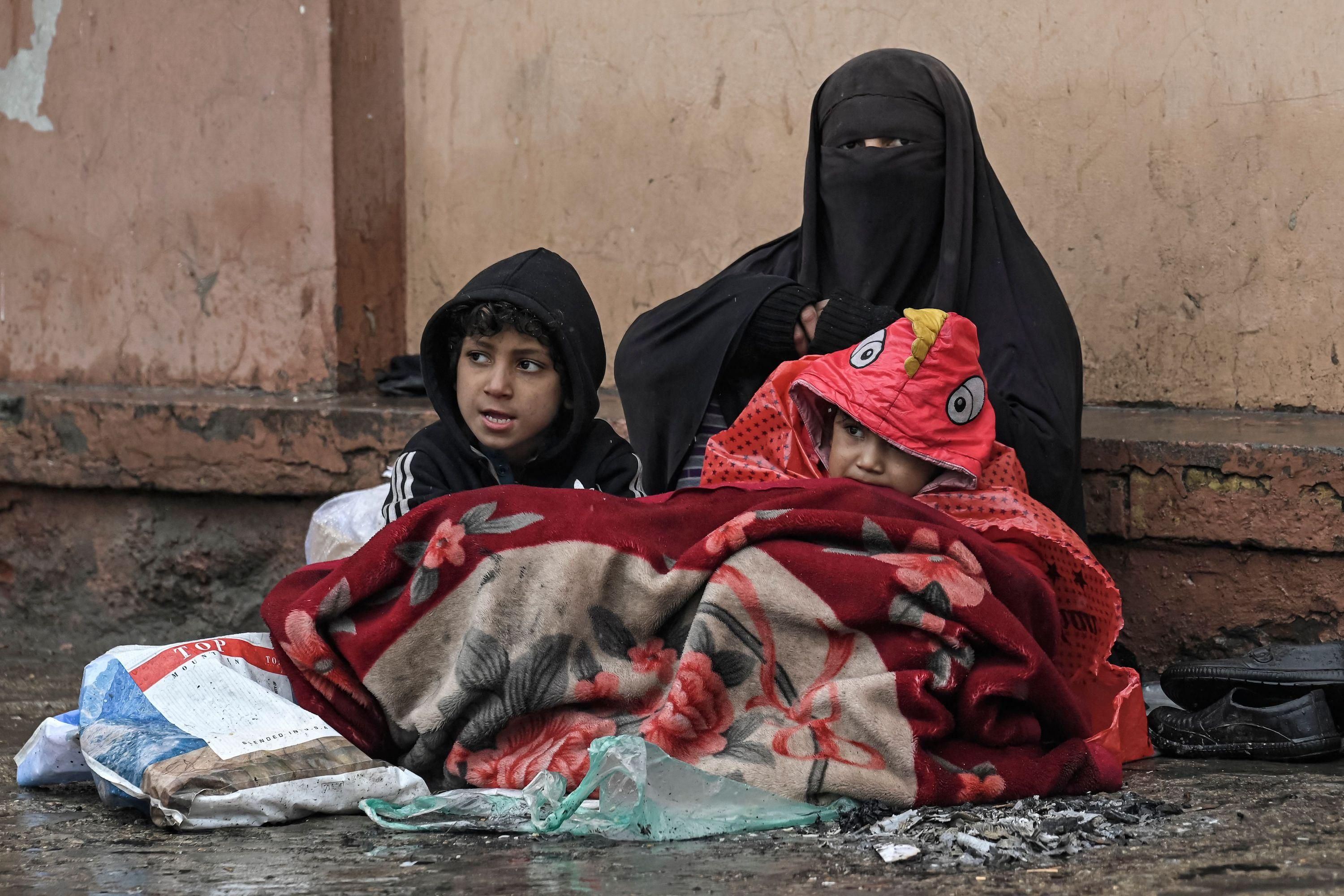 A burqa-clad Afghan woman sits next to a boundary wall with her children as she seeks alms from people passing by along a road in Kabul on January 8, 2022