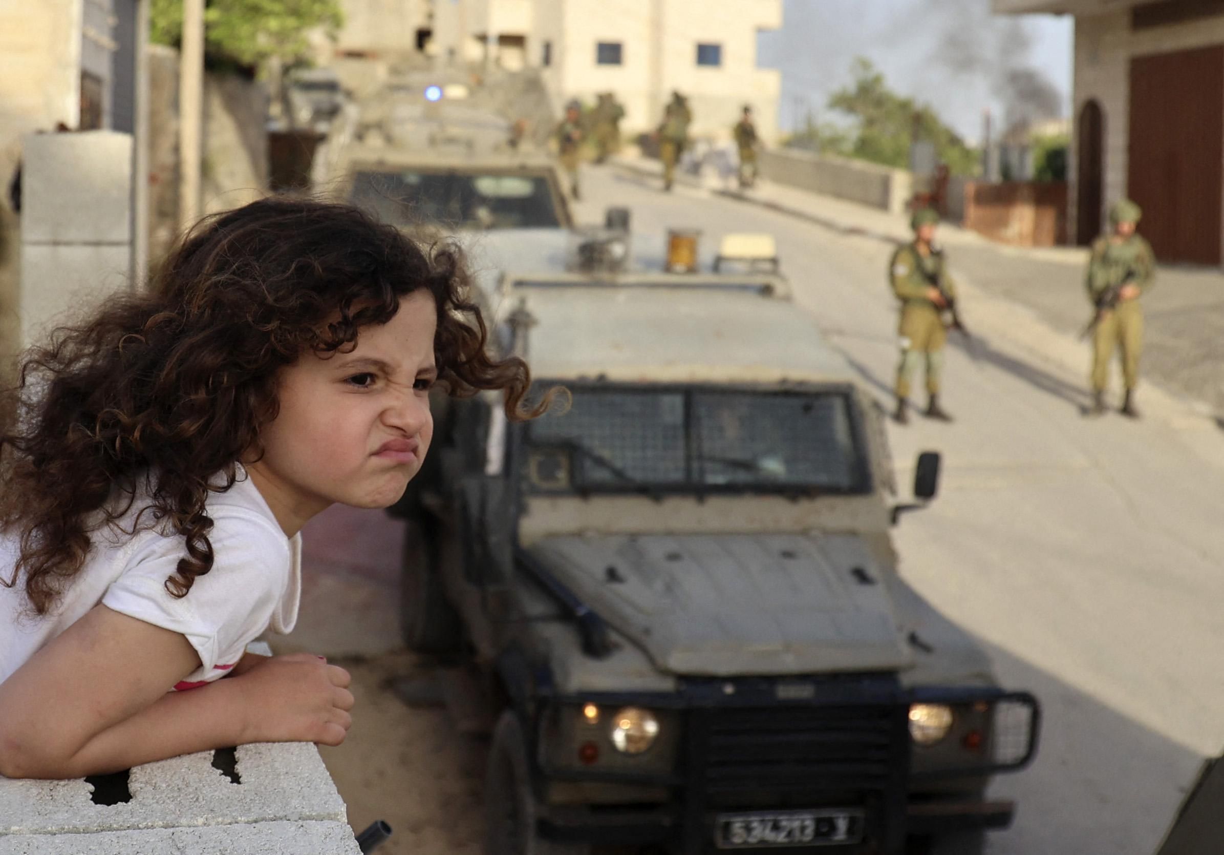 Palestinian girl looking on as Israeli soldiers conduct operation