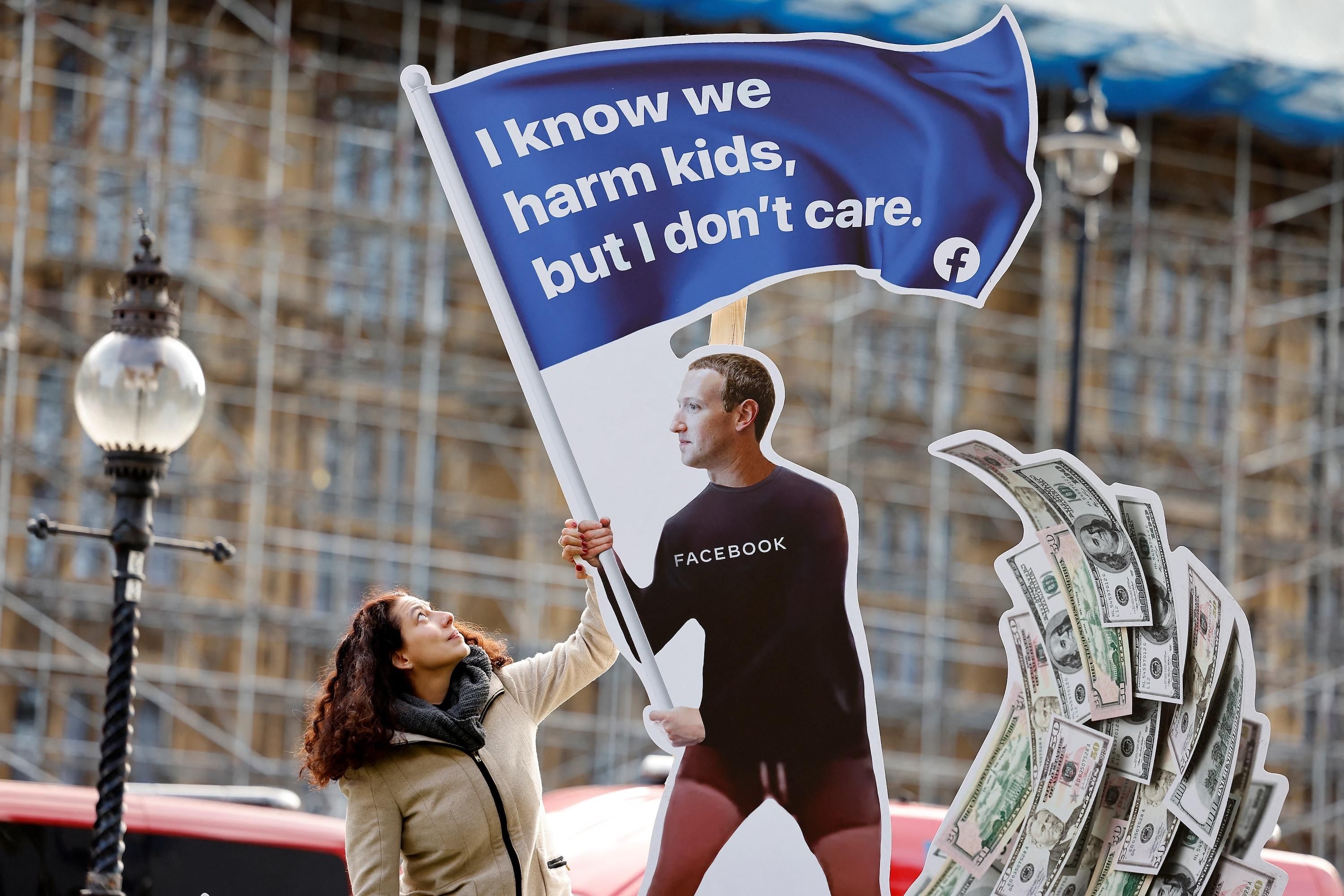 A demonstrator poses with an installation depicting Facebook founder Mark Zuckerberg surfing on a wave of cash and surrounded by distressed teenagers, during a protest opposite the Houses of Parliament in central London on October 25, 2021, as Facebook whistleblower Frances Haugen is set to testify to British lawmakers. (Photo by Tolga Akmen / AFP) 
