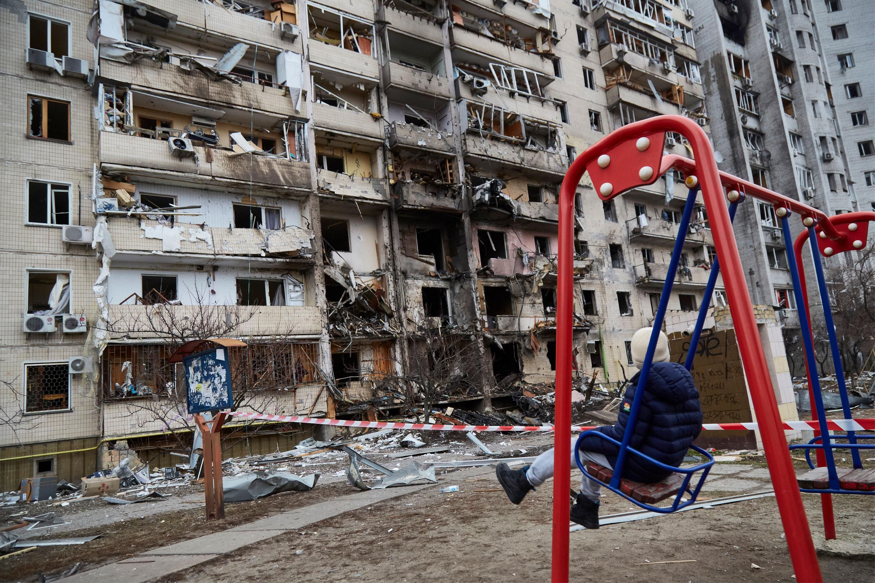 child on swing in front of destroyed building