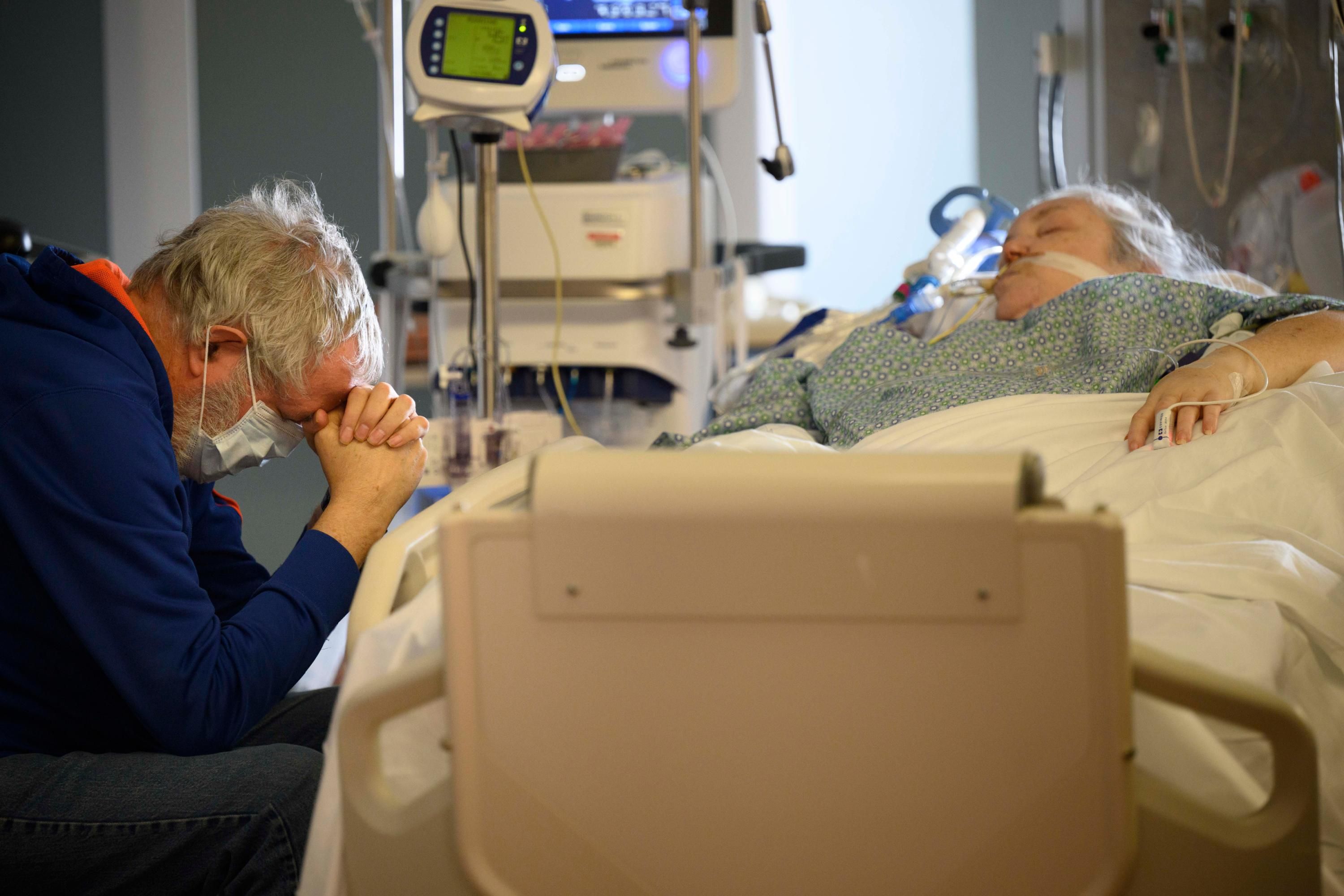 The husband of a Covid-19 patient prays at her bedside
