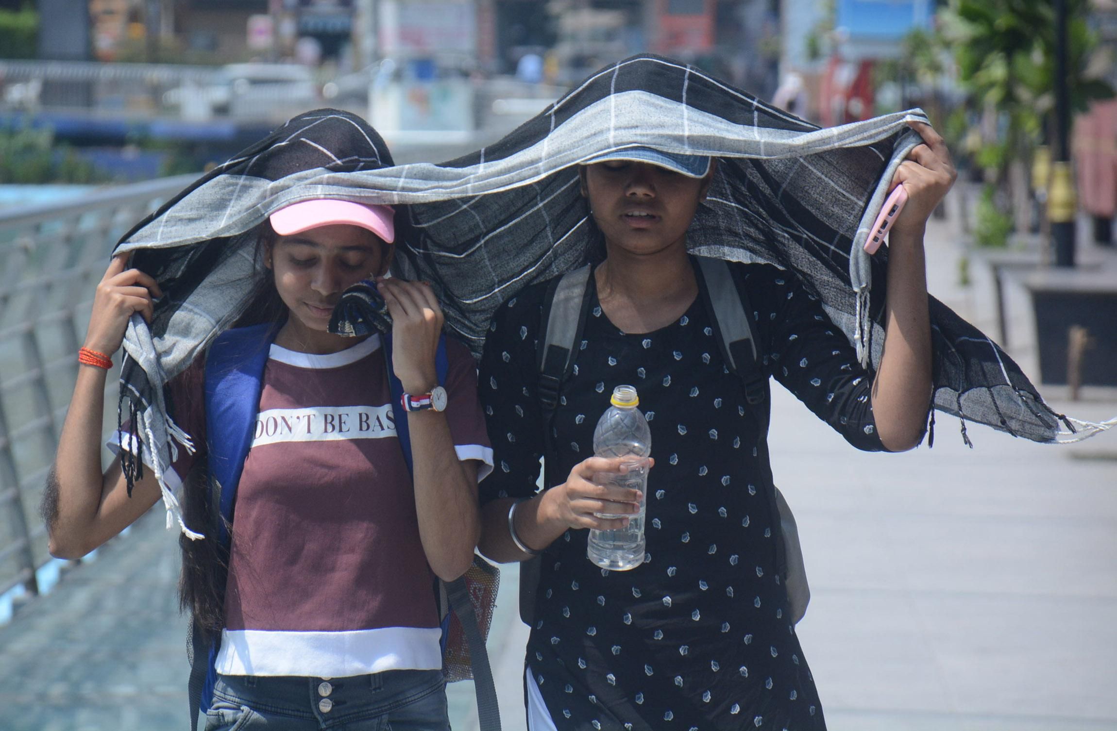 Two young girls cover their heads as they walk while drinking water in the scorching afternoon heat on April 25, 2022 in Mumbai, India.