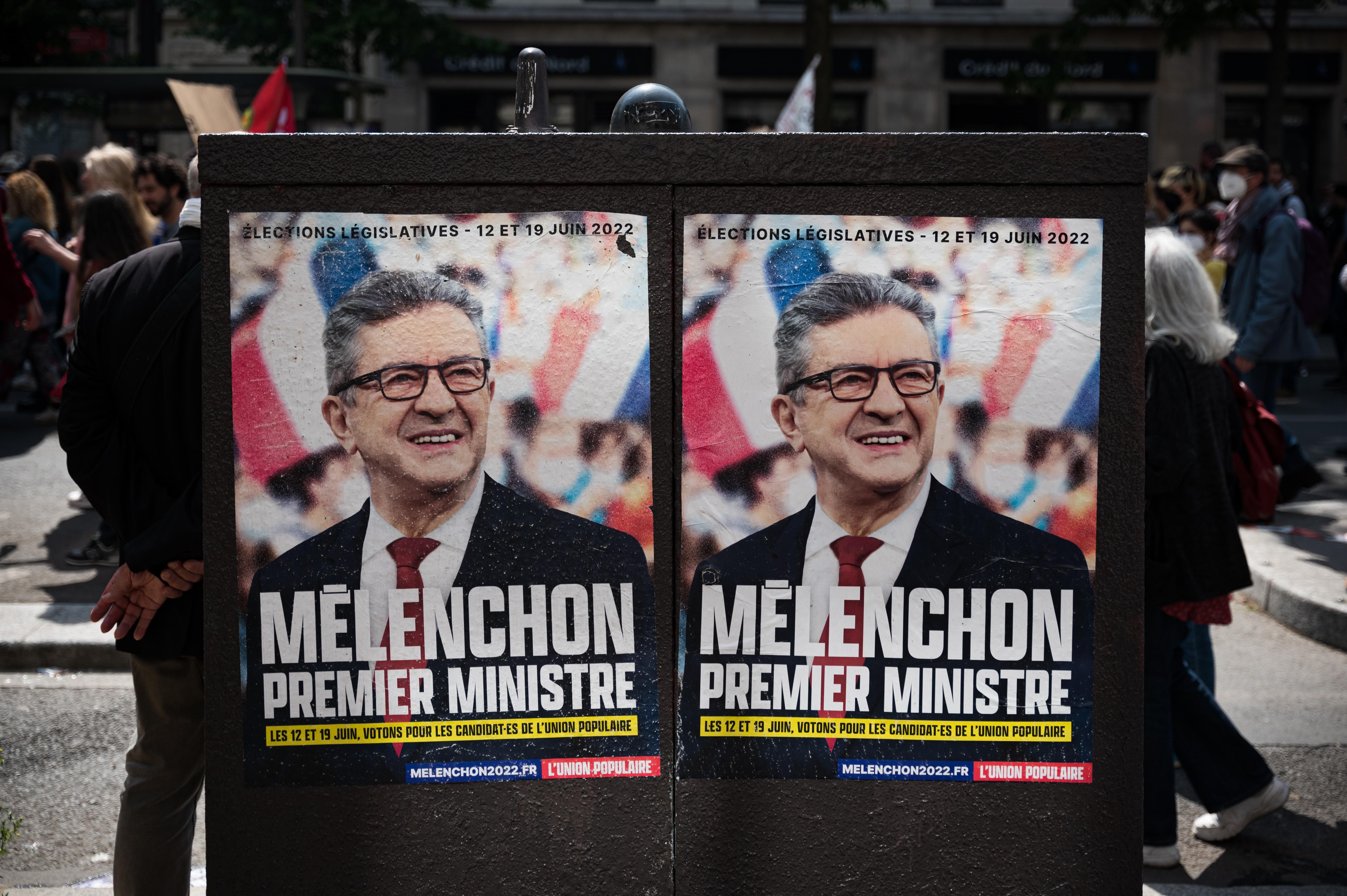 During a May Day demonstration in Paris, people walk past campaign posters for the June 2022 legislative election that portray left-wing MP Jean-Luc Mélenchon as prime minister.