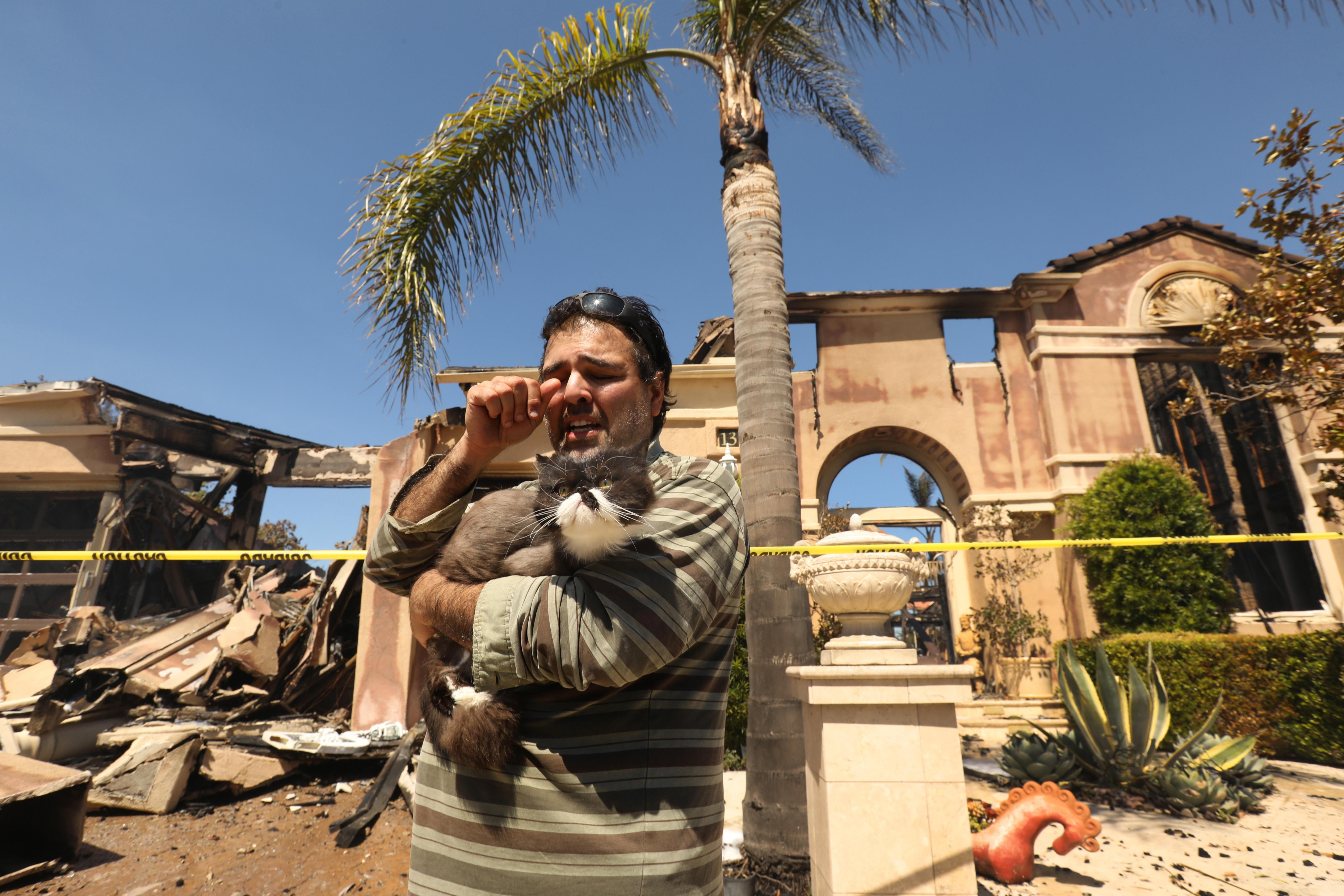 Sassan Darian, 38, holds his cat, Cyrus, as he assesses the damage outside his father's home on Coronado Pointe in California on May 12, 2022