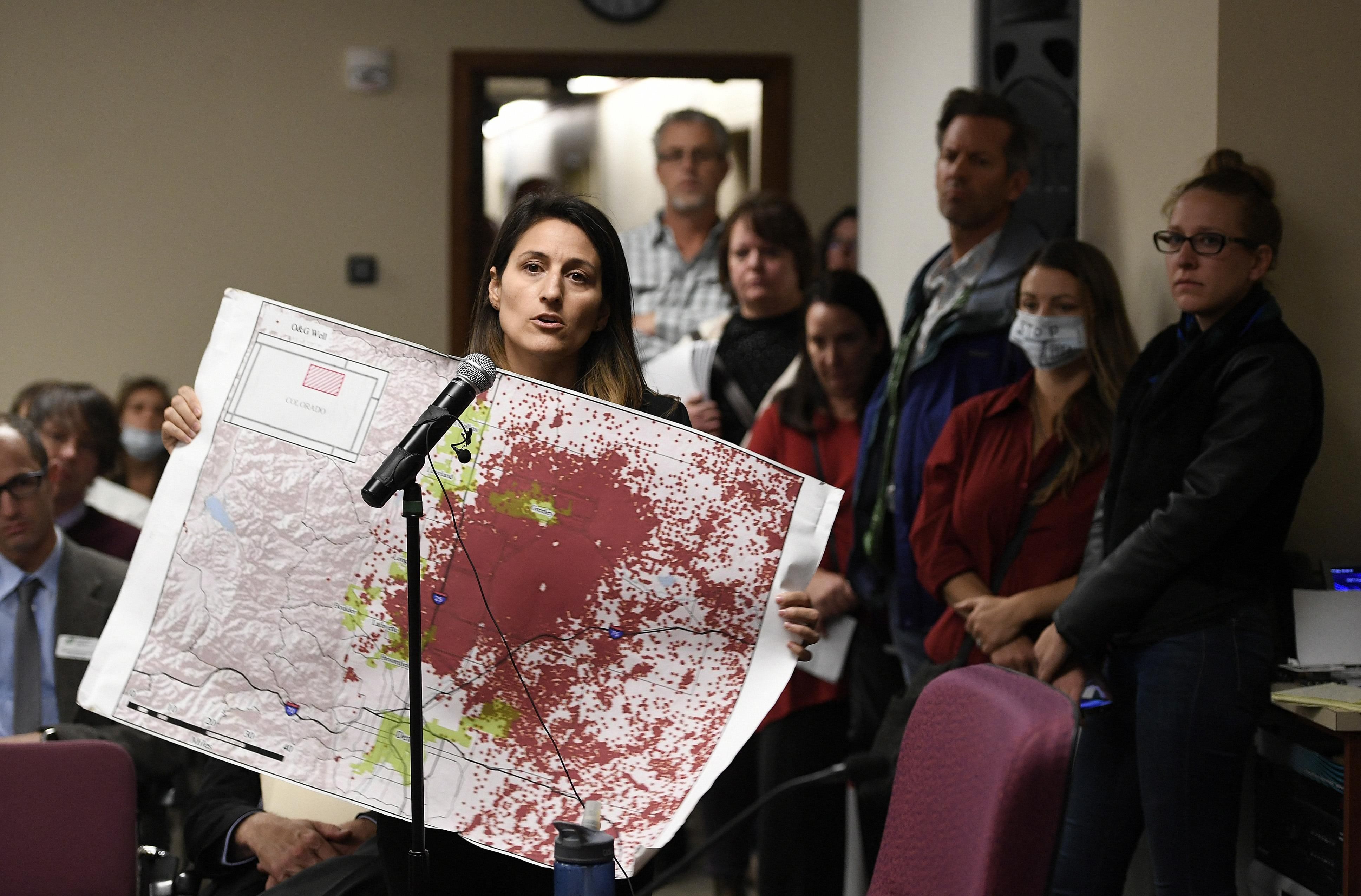 Lauren Petrie, of Food & Water Watch, holds up a map showing all of the fracking sites along the Front Range as she addresses members of the Colorado Oil and Gas Conservation Commission during a public comment session on October 30, 2017 in Denver.