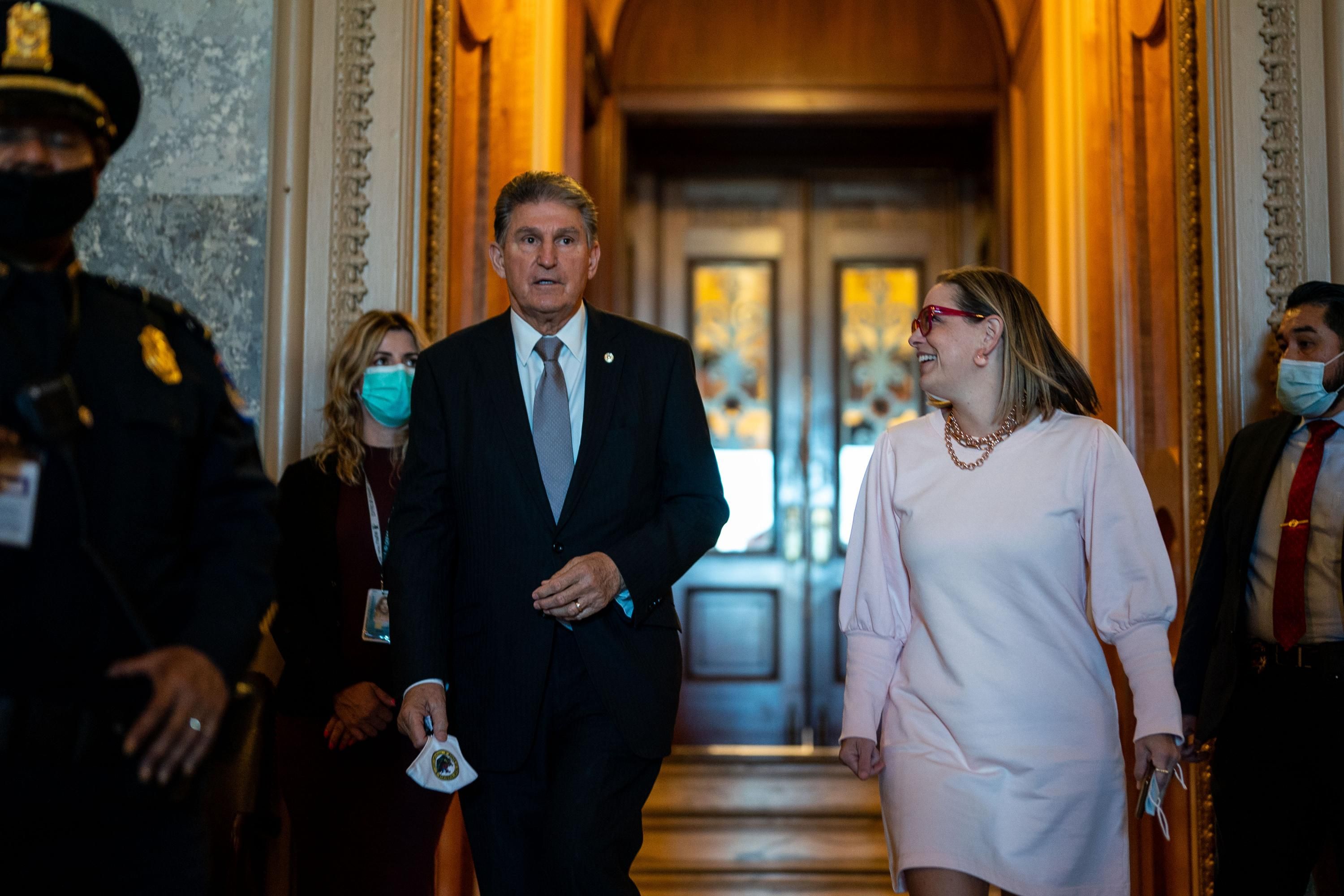 Sens. Joe Manchin and Kyrsten Sinema walk in the Senate hallway