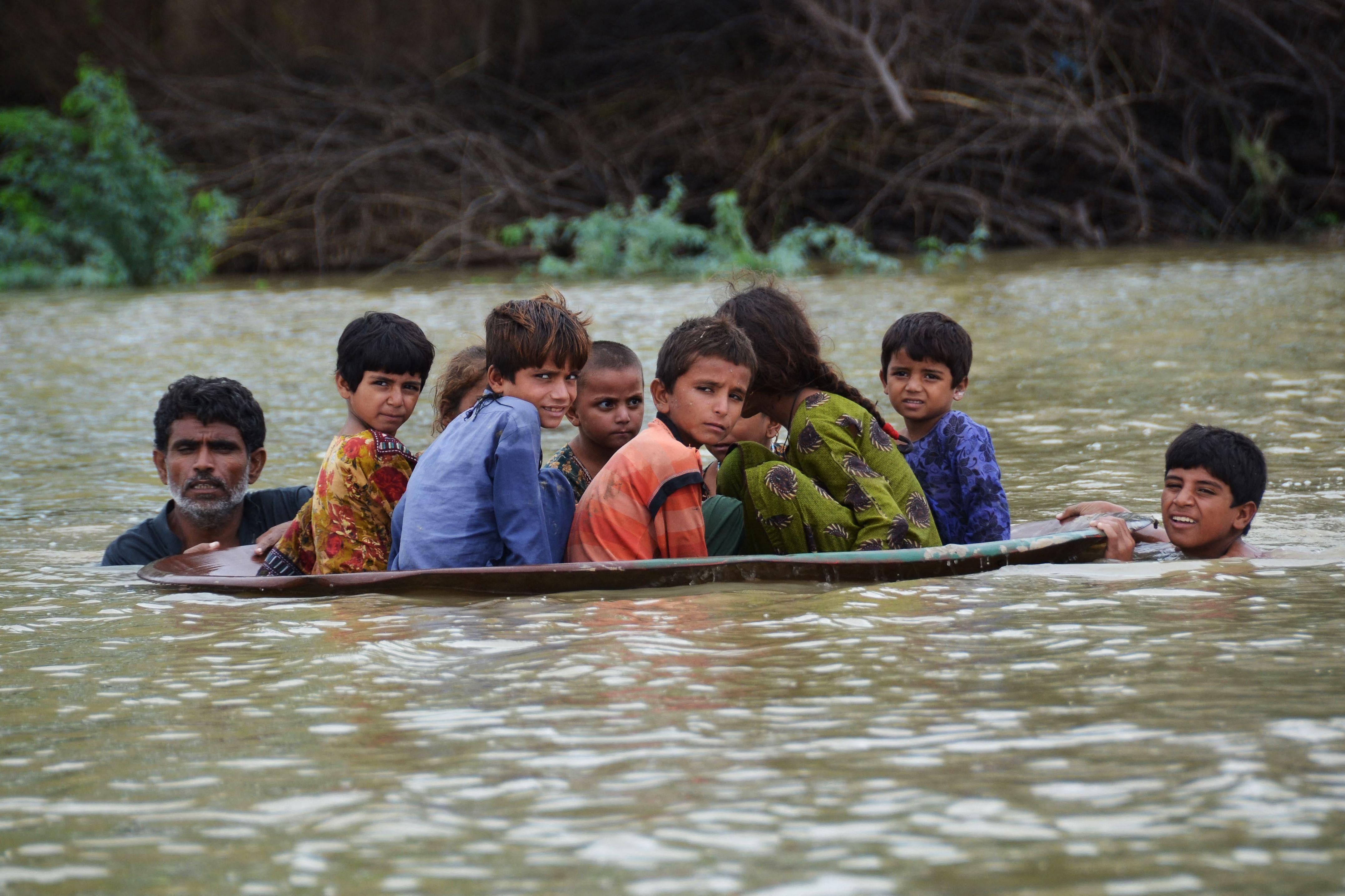 Children are helped across a flooded area in Pakistan's Balochistan province after catastrophic monsoon rains continued on August 26, 2022. 