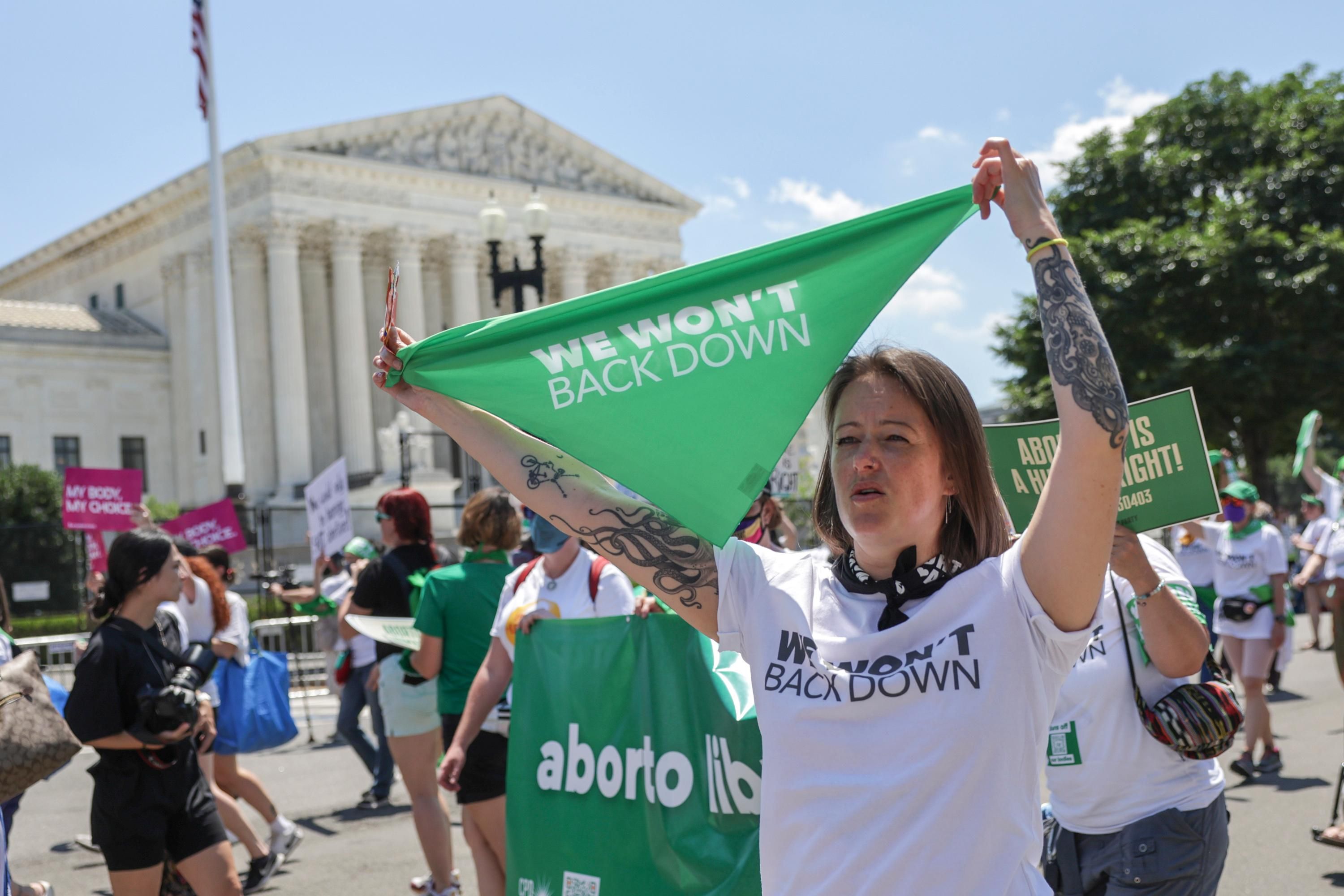 Woman holds banner reading, "We won't back down" outside Supreme Court