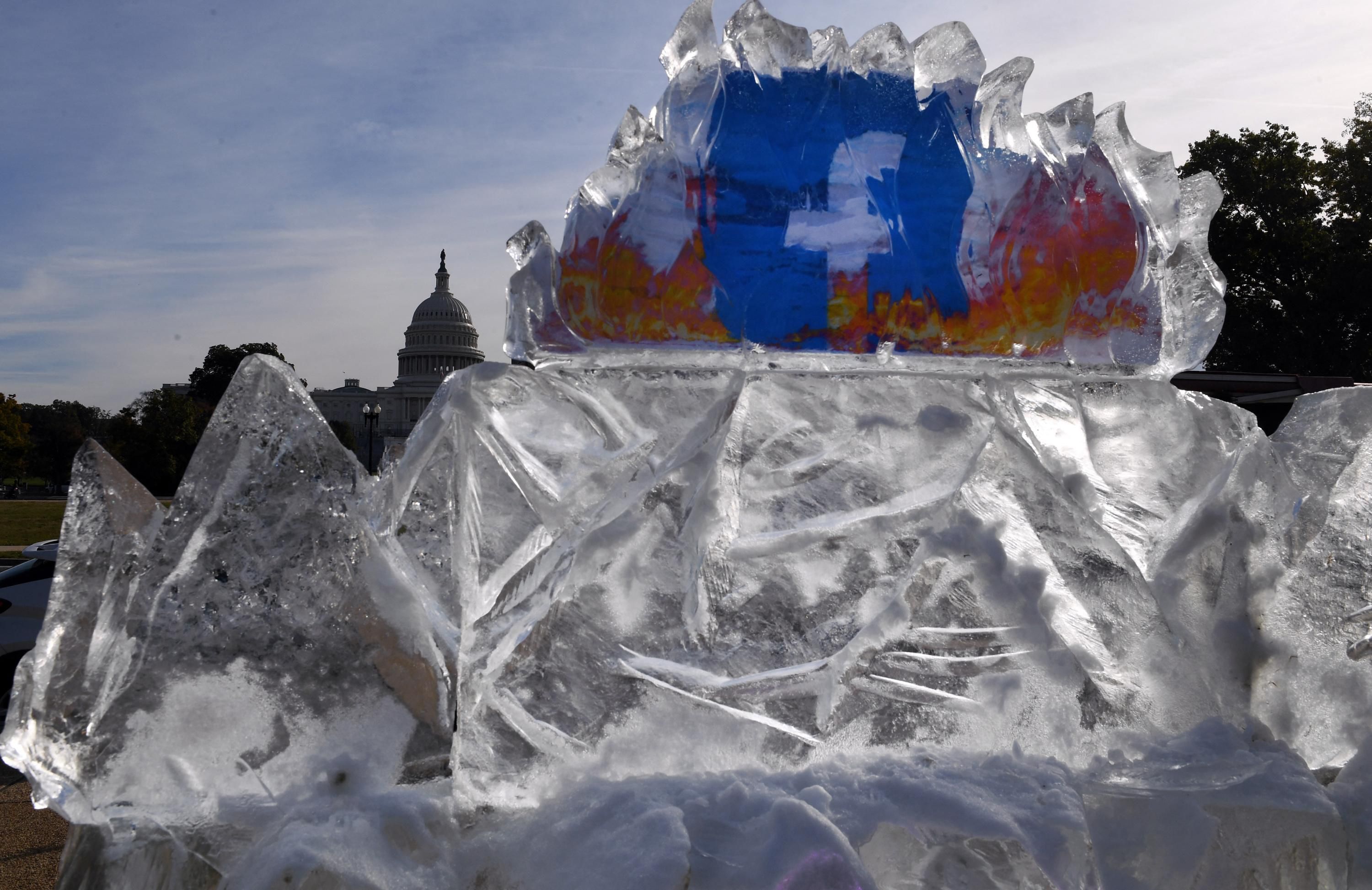 Climate activists display a burning Facebook logo in a melting block of ice