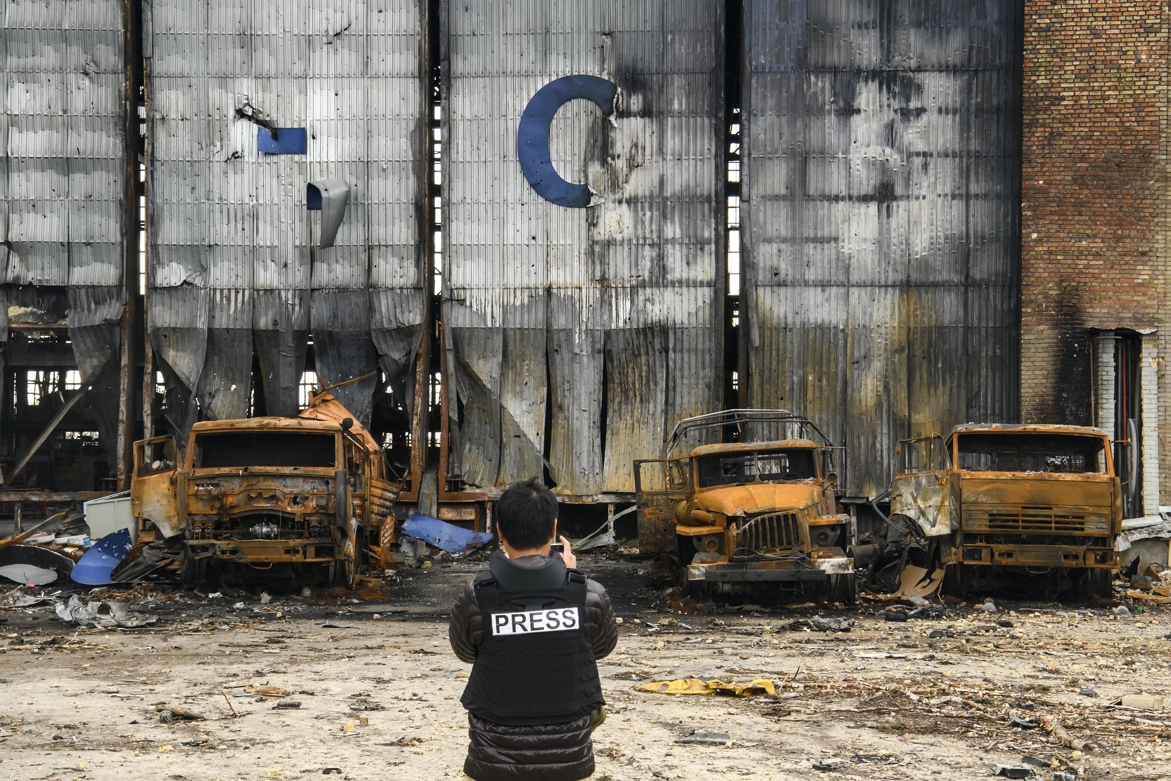 Reporter standing before burned out trucks during war in Ukraine