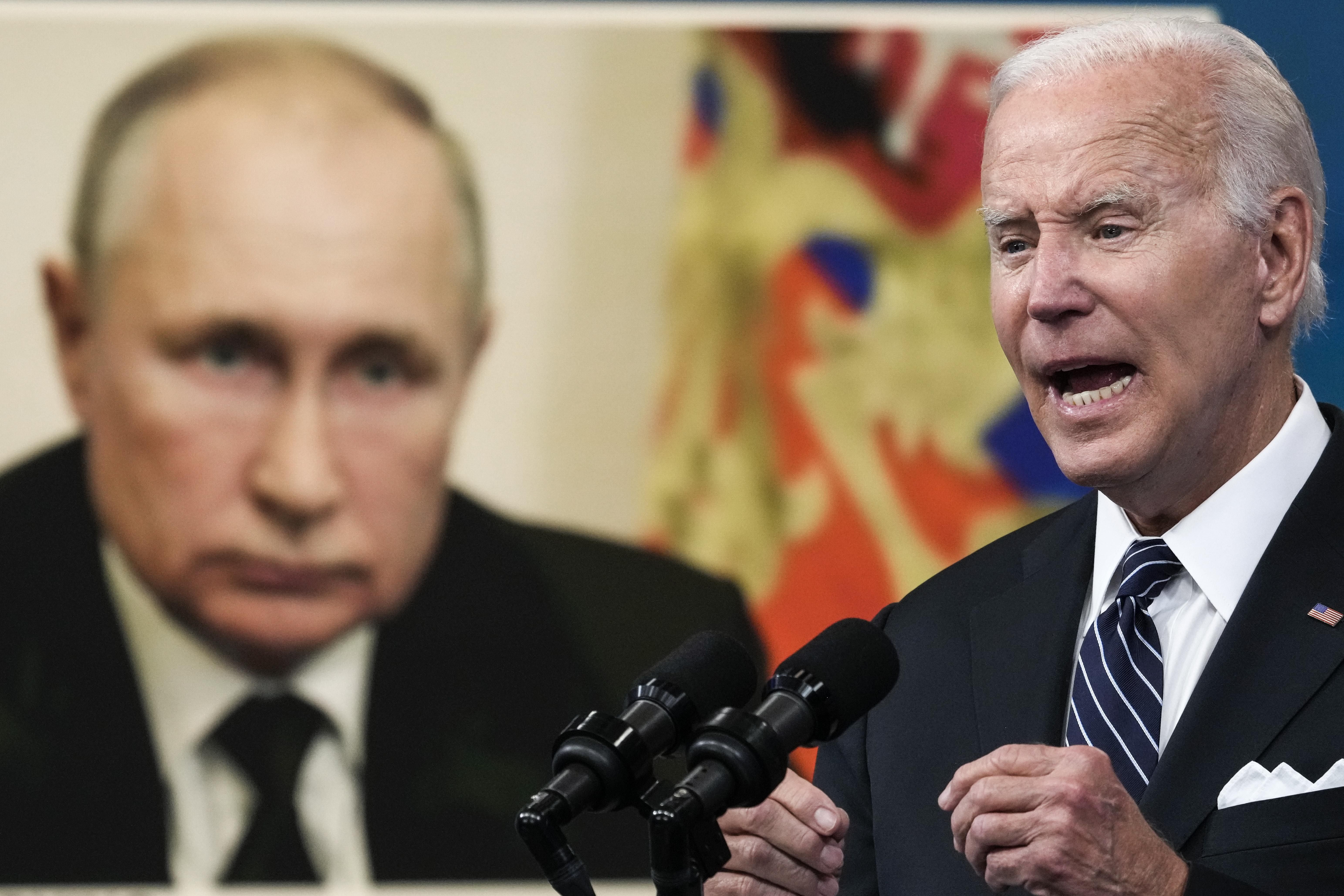 Joe Biden speaking in front of a photo of Vladimir Putin