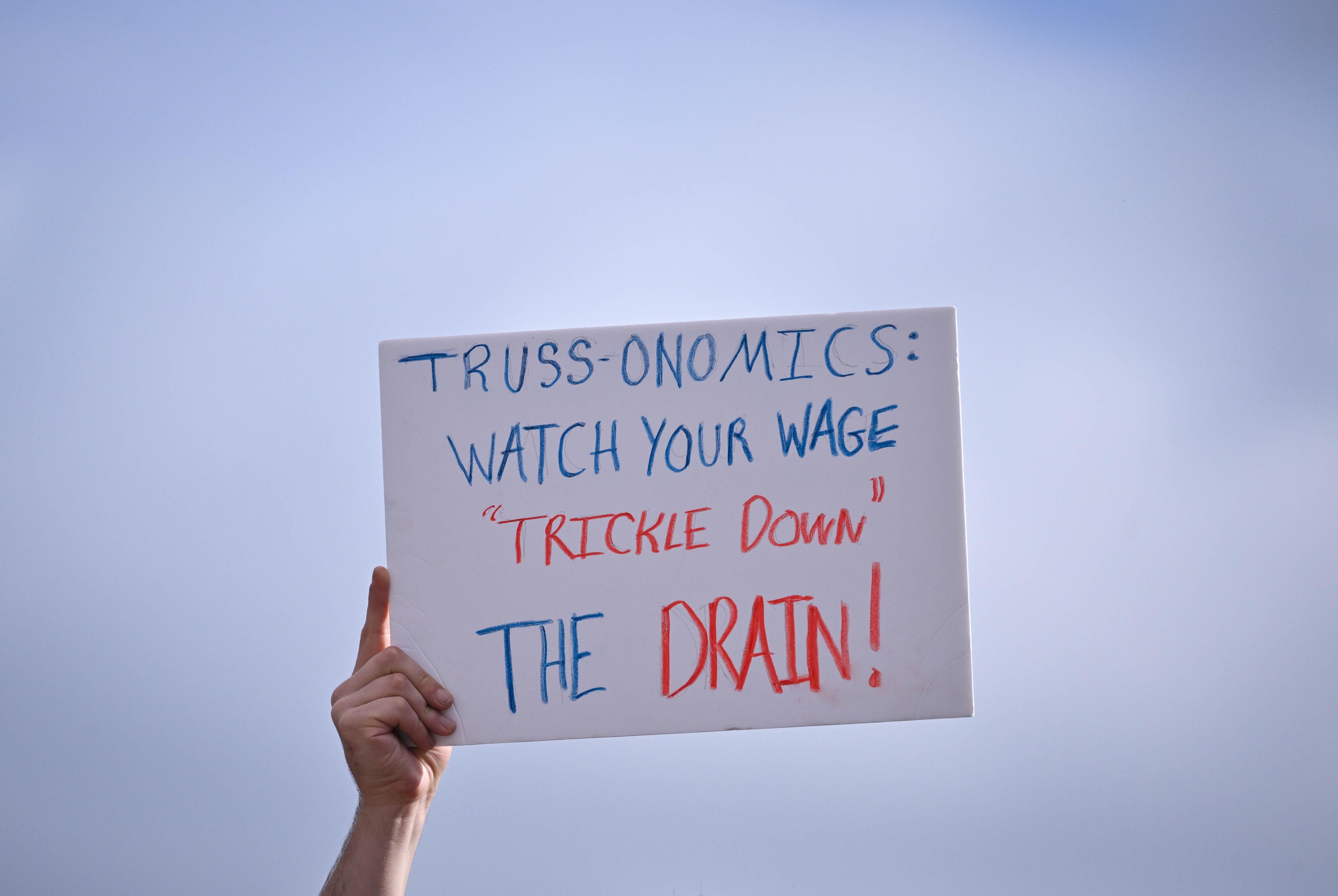 Signs reads "Truss-onomics: Watch your wage 'trickle down' the drain!"
