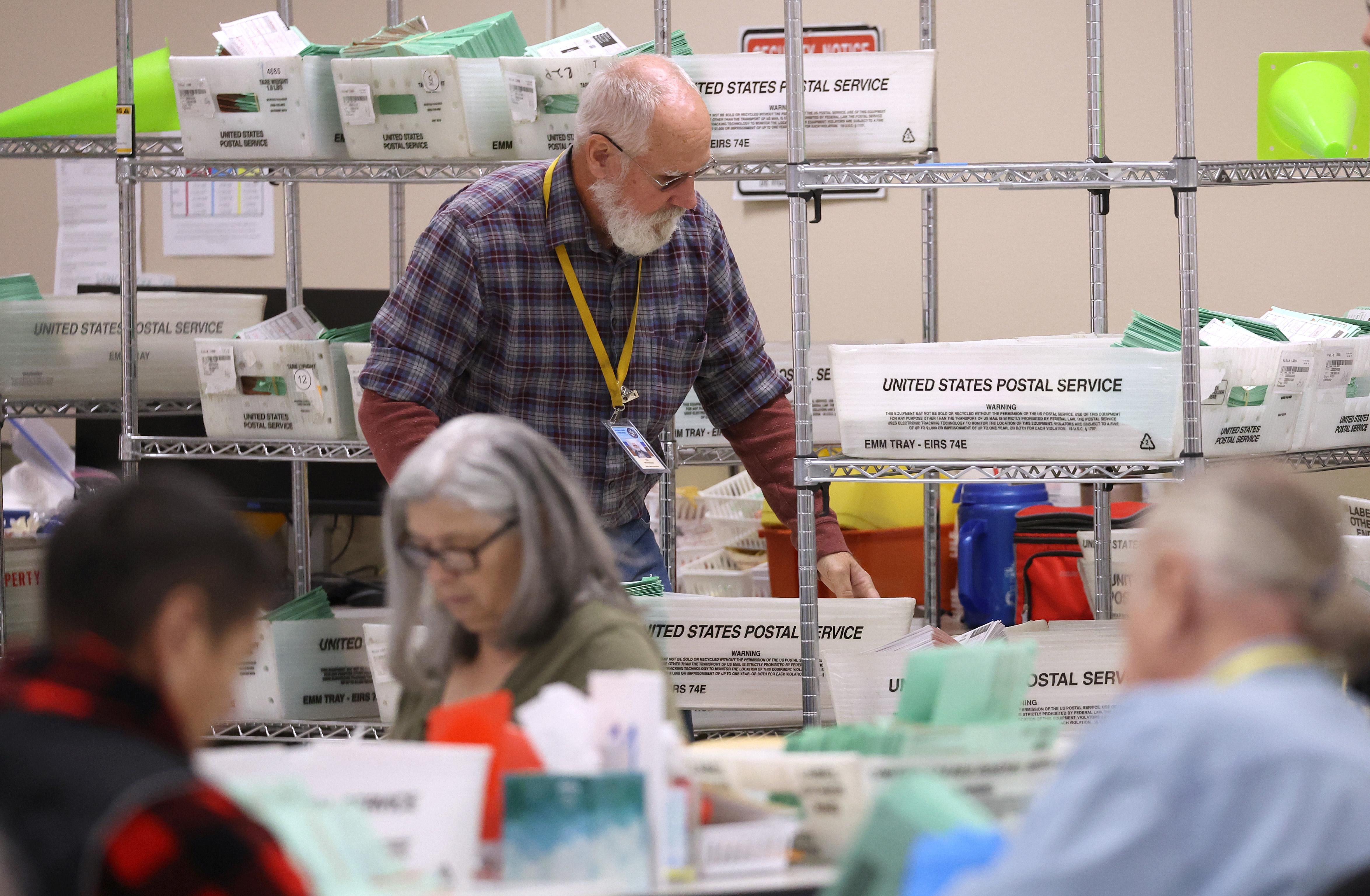 An elections worker carries a tray filled with mail-in ballots at the Maricopa County Tabulation and Election Center on November 6, 2022 in Phoenix, Arizona.