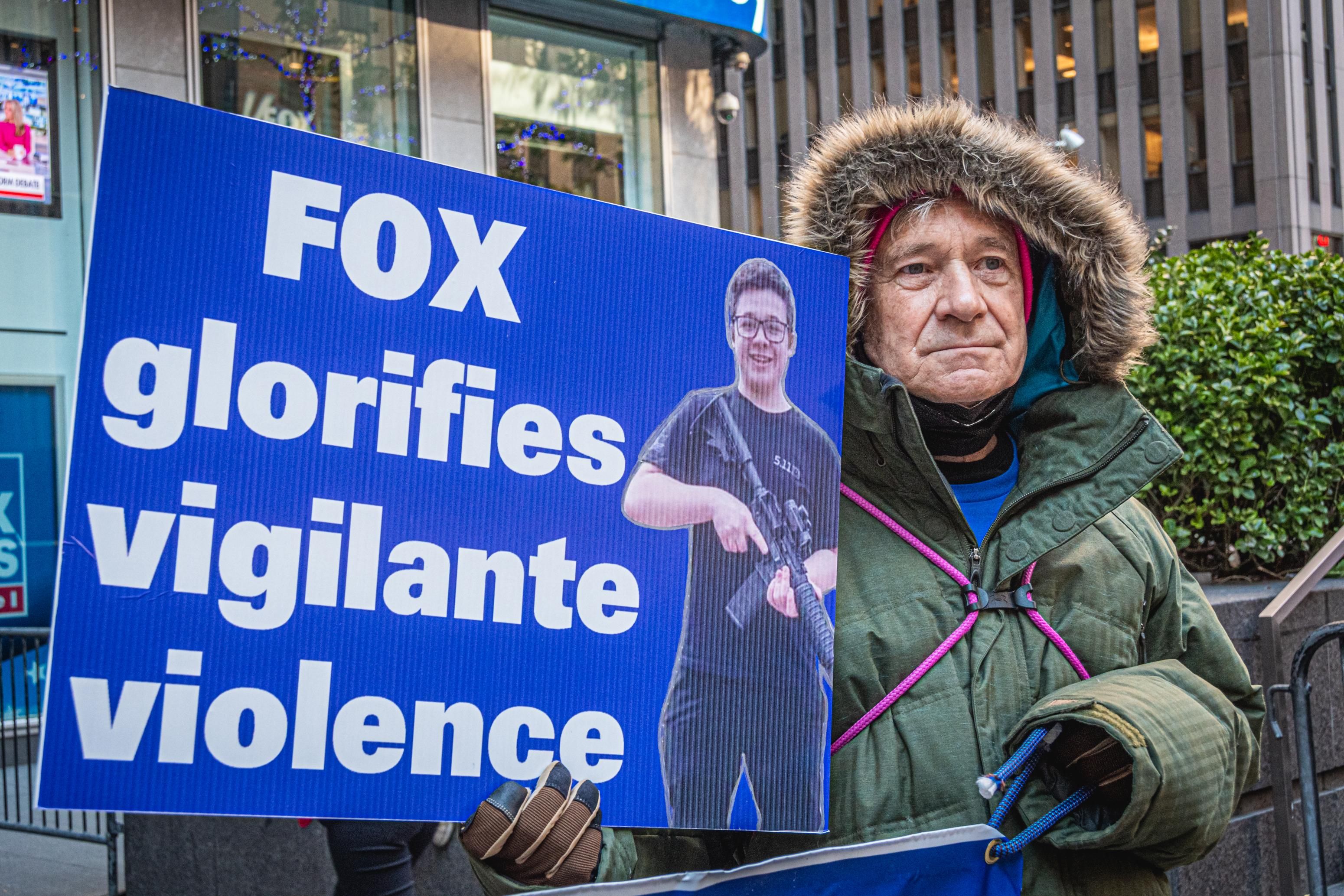 Protesters holds sign featuring Kyle Rittenhoouse. The sign says: 
