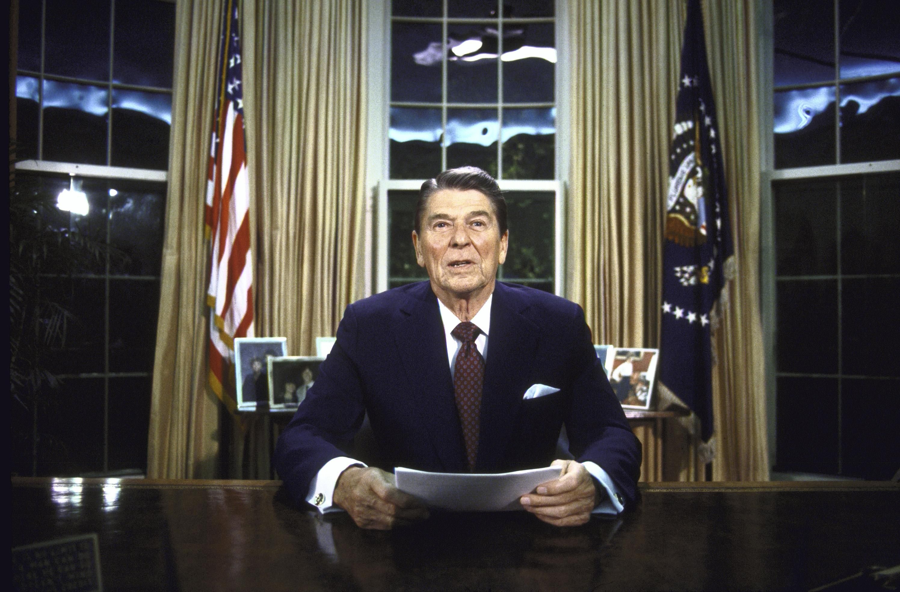 Then-President Ronald Reagan seated at his desk in the Oval Office