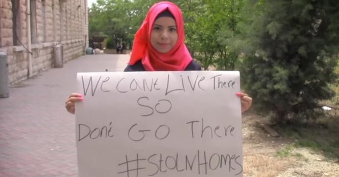 A young woman holds a sign urging Airbnb to stop listing homes in occupied Palestinian land. 