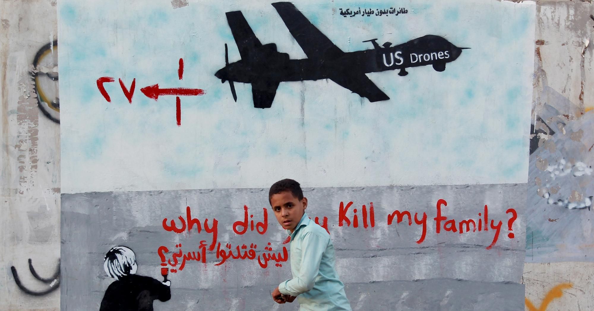 A Yemeni boy (C) walks past a mural depicting a U.S. drone and reading " Why did you kill my family?" on December 13, 2013 in the capital Sanaa.