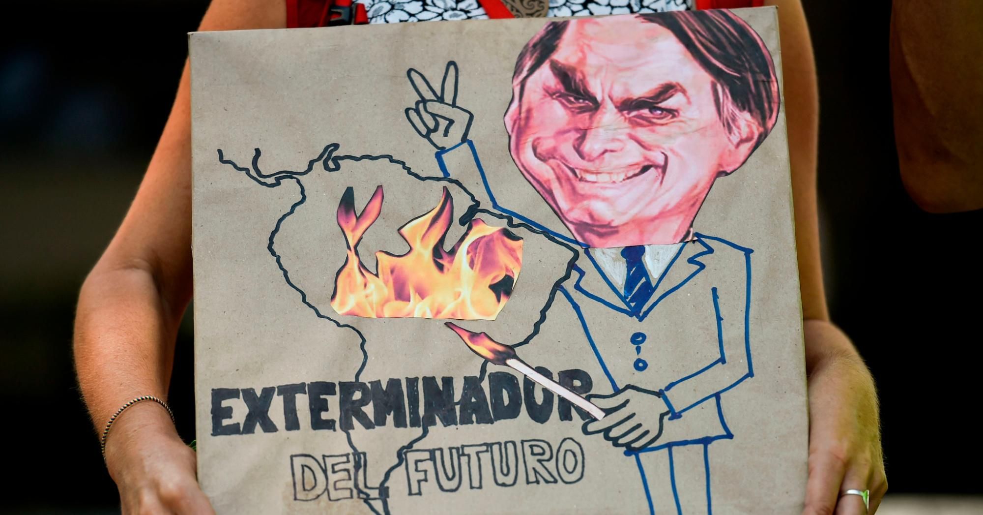 A climate change activist holds a sign depicting Brazilian President Jair Bolsonaro with the slogan "Exterminator of the Future" during a protest against the Brazilian leader over the fires in the Amazon rainforest on August 23, 2019. 
