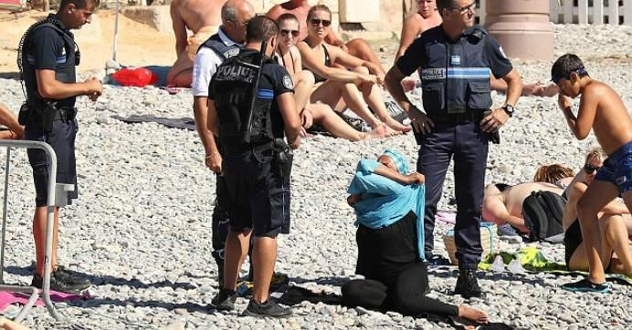 A female beachgoer in Nice, France is surrounded by police and forced to remove a banned 'burkini.' (Photo: Vantagenews.com)