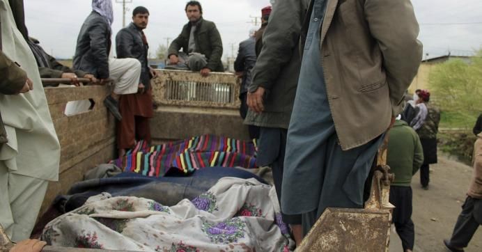 Men stand over bodies during a protest in Kunduz province north of Afghanistan, Saturday, Mar. 23, 2019. 