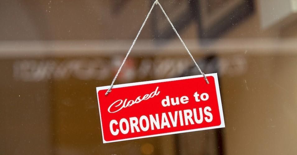 Red sign hanging at the glass door of a shop saying "Closed due to coronavirus."