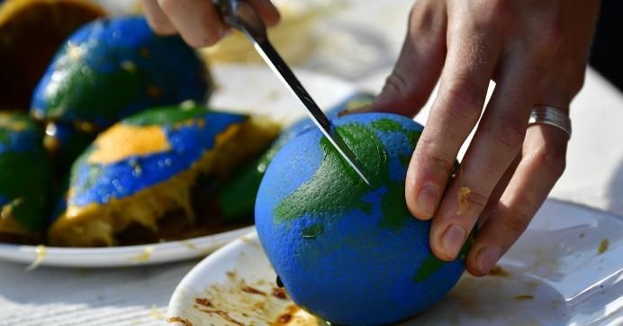An environmental activist cuts an orange, painted as a globe, during an event to mark the Earth Overshoot Day on August 1, 2018 in Berlin.
