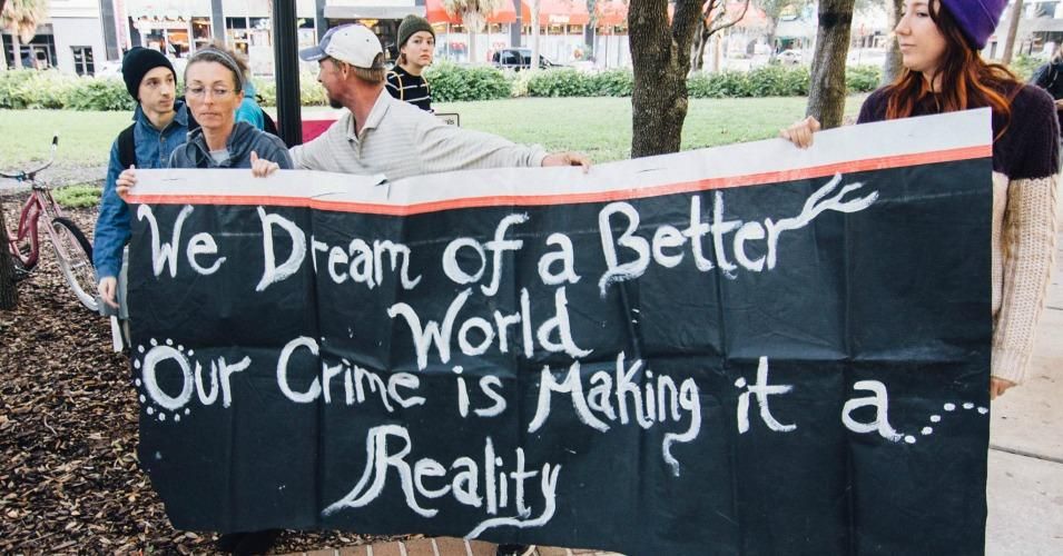 A banner held up by Food Not Bombs volunteers reads: "We dream of a better world/our crime is making it a reality"