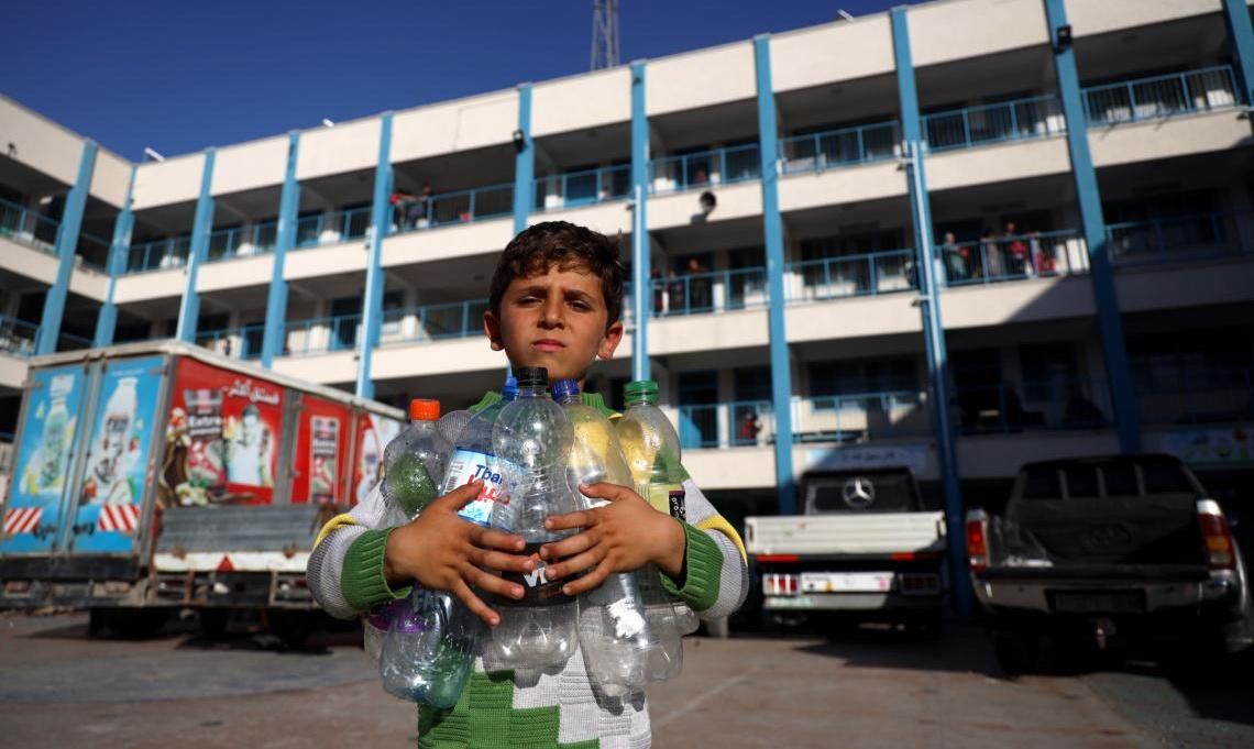 A boy in Gaza holds empty water bottles as he looks for a place to fill them with clean drinking water.
