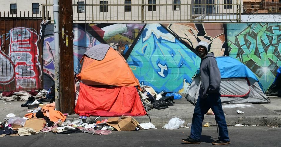 A pedestrian walks past tents and trash 