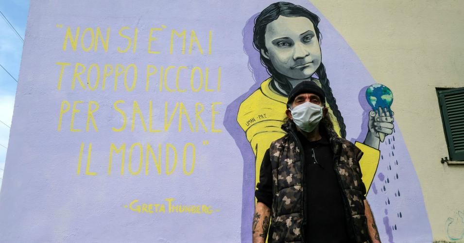 A resident wearing a face mask stands next to a mural featuring Swedish climate activist Greta Thunberg and her quote "You're never too young to save the world" on March 30, 2020 in the Trullo district of Rome during Italy's lockdown in response to the coronavirus pandemic.