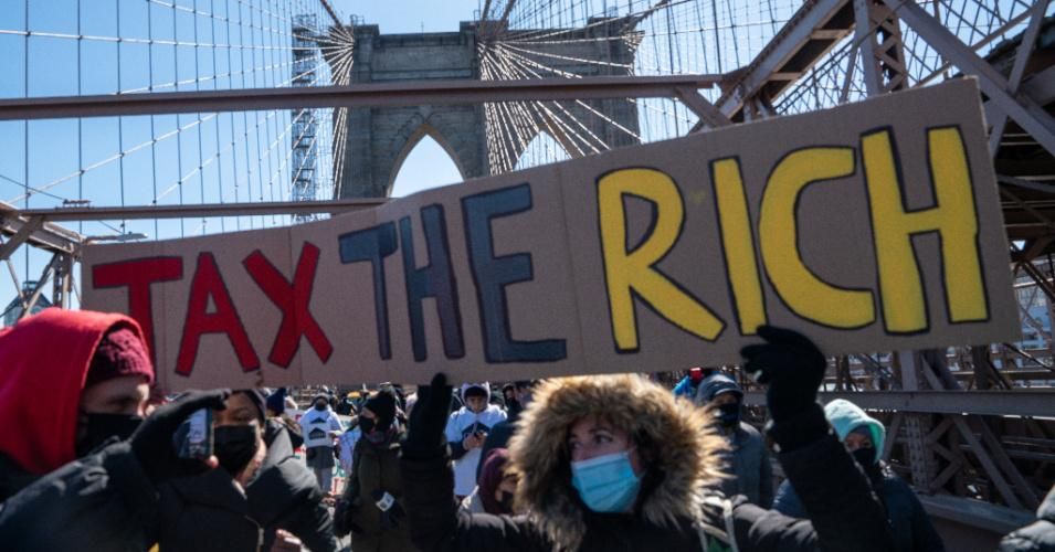 Protestors march across the Brooklyn Bridge holding a sign to "tax the rich" on March 5, 2021 in New York City.