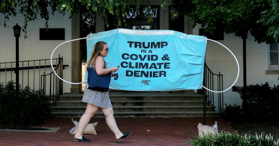 A woman walks past a protest banner demanding President Trump stop denying the science behind the Covid-19 pandemic and climate change set up in front of the Republican National Convention Headquarters on August 24, 2020 in Washington, D.C. (Photo: Jemal Countess/Getty Images for Climate Power 2020)