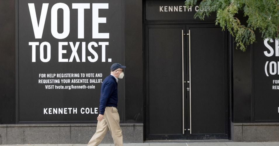 A man wearing a mask walks past a "vote to exist" sign displayed on the windows of Kenneth Cole on September 22, 2020 in New York City. (Photo: Alexi Rosenfeld/Getty Images)