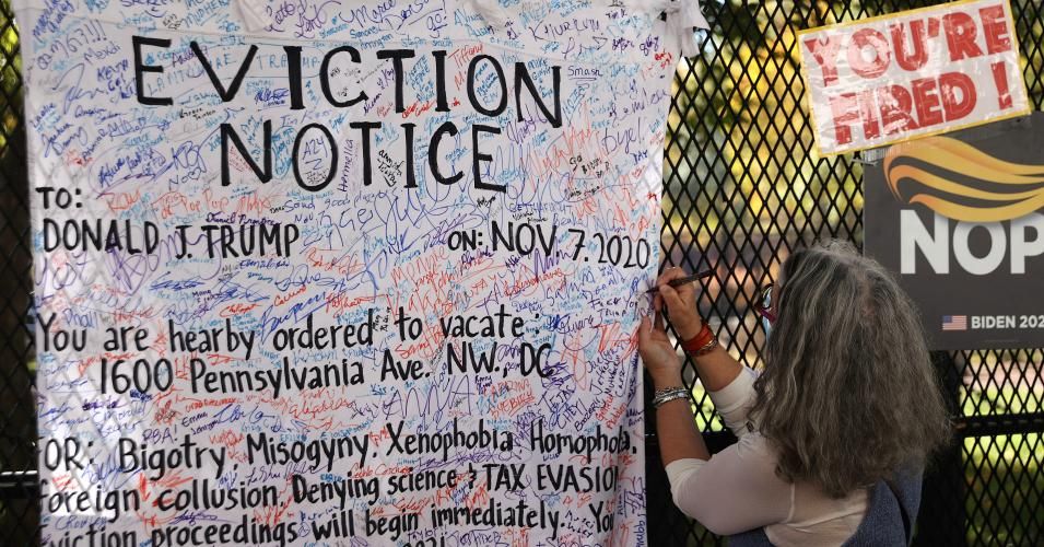 A woman signs an 'eviction notice' for President Donald Trump hanging on the security fence that surrounds the White House November 8, 2020 in Washington, D.C. (Photo: Chip Somodevilla/Getty Images)
