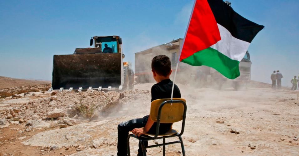 A Palestinian boy sits on a chair with a national flag as Israeli authorities demolish a school site in the village of Yatta, south of the West Bank city of Hebron on July 11, 2018. (Photo: Hazem Bader/AFP via Getty Images)