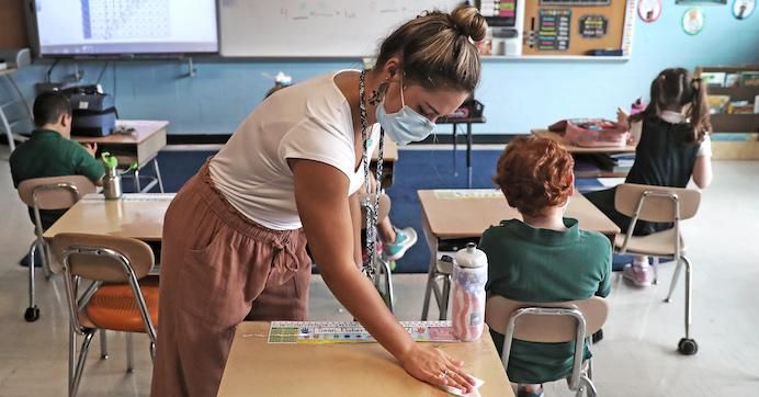 Second grade teacher Alice Rey sanitizers students' desks for snack time at South Boston Catholic Academy in South Boston on Sept. 10, 2020.