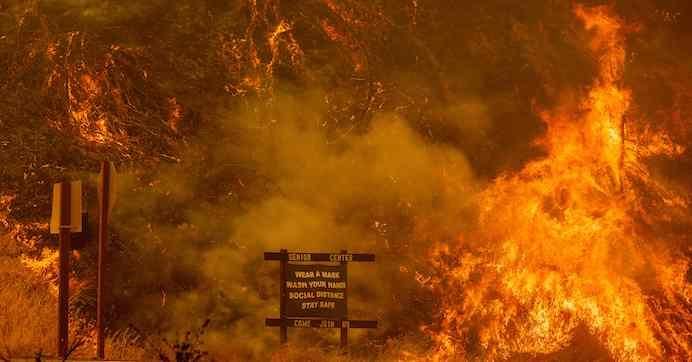 A sign warning people about Covid-19 is surrounded by flames during the Hennessey fire near Lake Berryessa in Napa, California on August 18, 2020. 