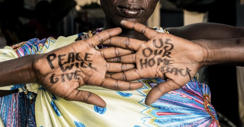  A woman named Mary at the Mangaten IDP Camp in South Sudan holds up her hands, which bear the message, "Peace will give us our home back." 