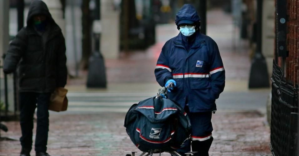 A U.S. Postal Service employee wears a mask and delivers mail in the wind and rain in Copley Square in Boston on April 9, 2020. 