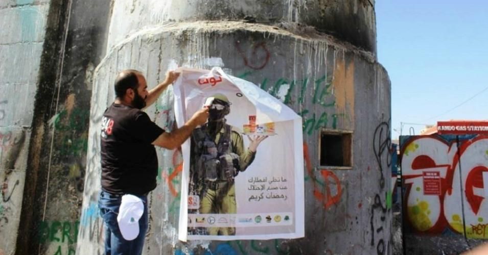 A campaigner in the West Bank puts up a poster in support of a BDS campaign. The Israeli government wants you to report this man. (Photo: Palestinian BDS Movement)