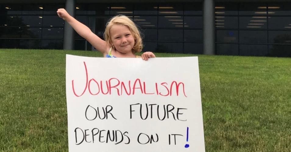 child holds up save the news sign