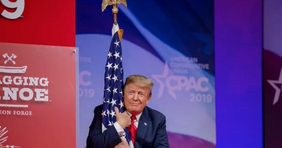 President Donald Trump hugs the U.S. flag during CPAC 2019 on March 2, 2019, in Washington, D.C. 
