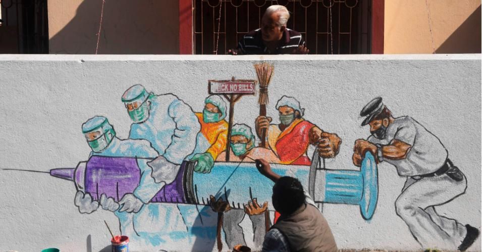 A resident watches an artist put the finishing touches on a mural depicting frontline workers carrying a Covid-19 vaccine in Kolkata on January 2, 2021. (Photo: Dibyangshu Sarkar/AFP via Getty Images)