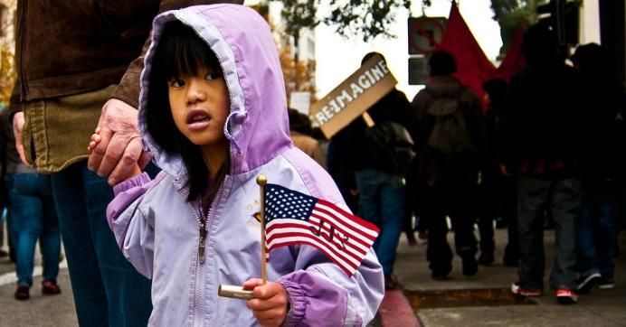 A young girl holds a flag in front of a sign reading 'Re-imagine.'