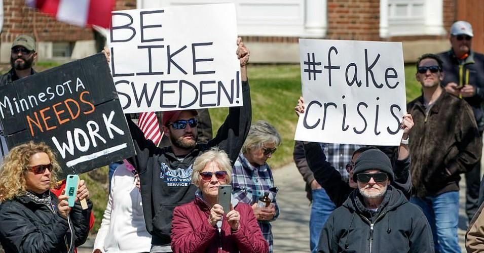 A right-wing protester holds a sign which reads "Be like Sweden" while another called the coronavirus pandemic a "fake crisis" during an April anti-lockdown demonstration in Minnesota. 
