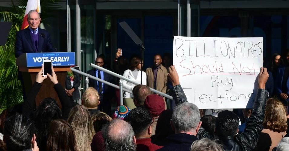 Democratic presidential candidate Mike Bloomberg speaks during the kickoff of his "Get it Done Express" bus tour as a protester holds up a sign reading "Billionaires Should Not Buy Elections" at the Dollarhide Community Center in Compton, California on February 3, 2020. (Photo: Frederic J. Bown / AFP/Getty Images)